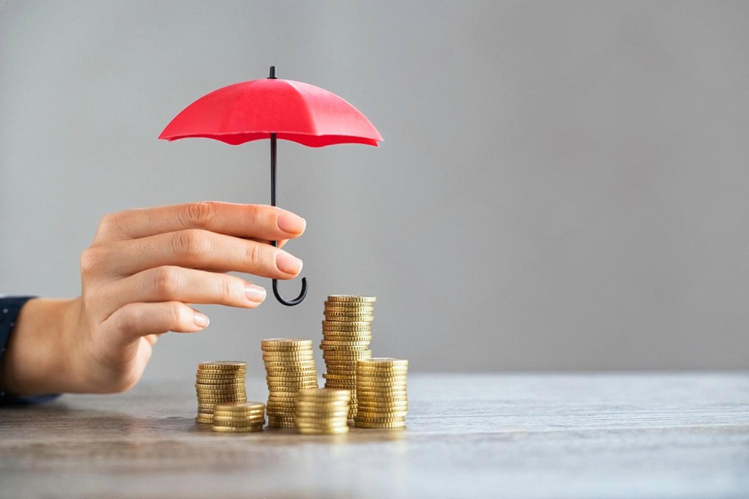 Hand holding a small red umbrella over stacks of gold coins, symbolising financial protection from internal business risks
